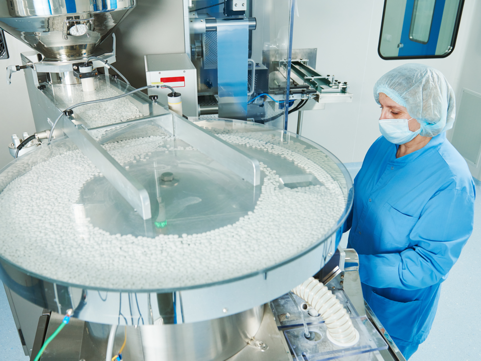 Žena vo farmaceutickom laboratóriu pred strojom na výrobu tabliet