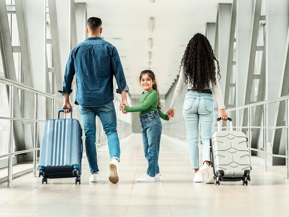 Three people — parents and a child — walking through an airport terminal with suitcases.