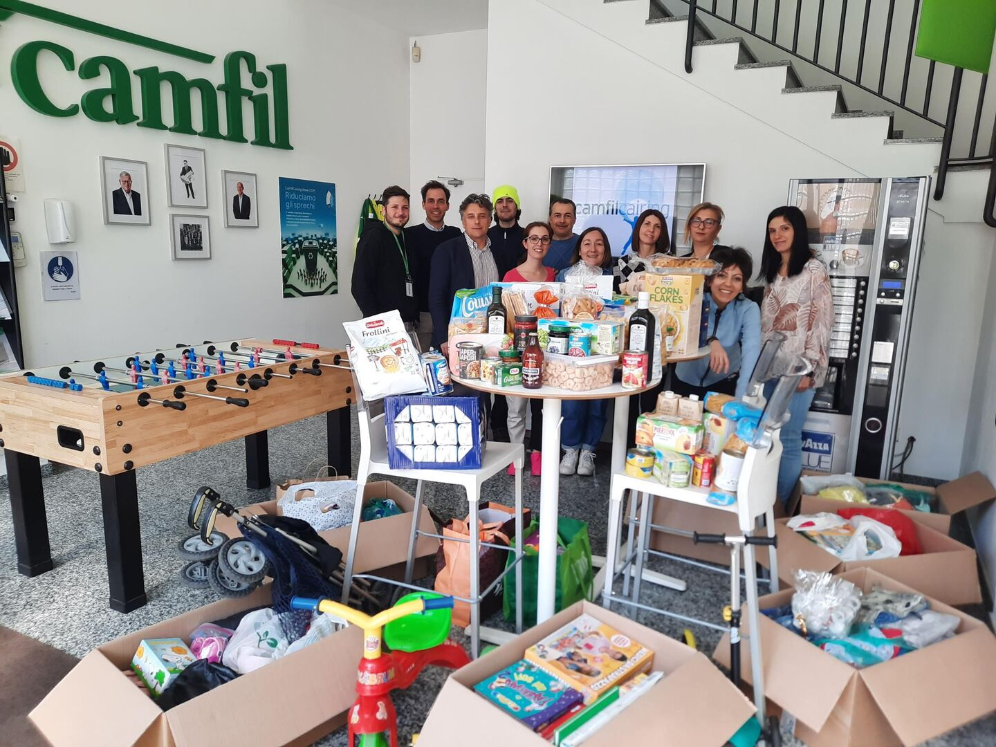 Team riunito nella reception di Camfil Italia durante un’iniziativa solidale, con raccolta di alimenti, prodotti per la cura e giochi destinati a una donazione.