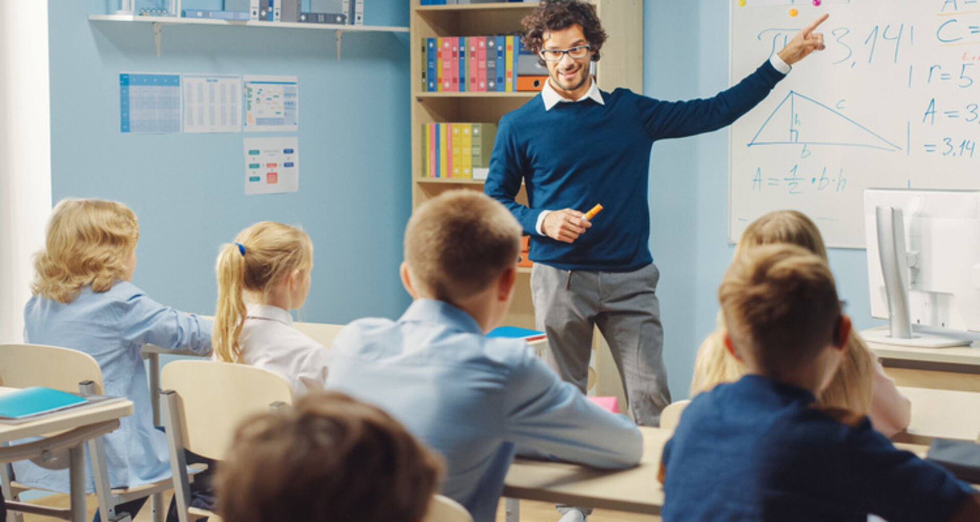 Caring Teacher Explains Lesson to a Classroom Full of Bright Diverse Children. In Elementary School with Group of Smart Multiethnic Learning Science, Listening to a Teacher with Great Interest