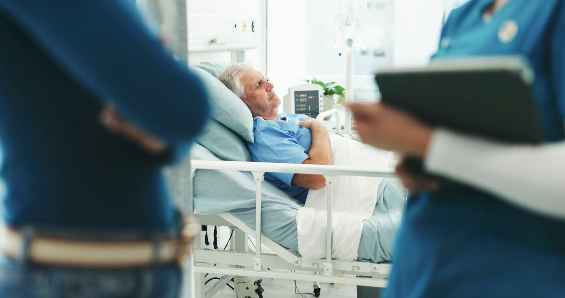 Man in hospital bed with doctors talking outside of the room