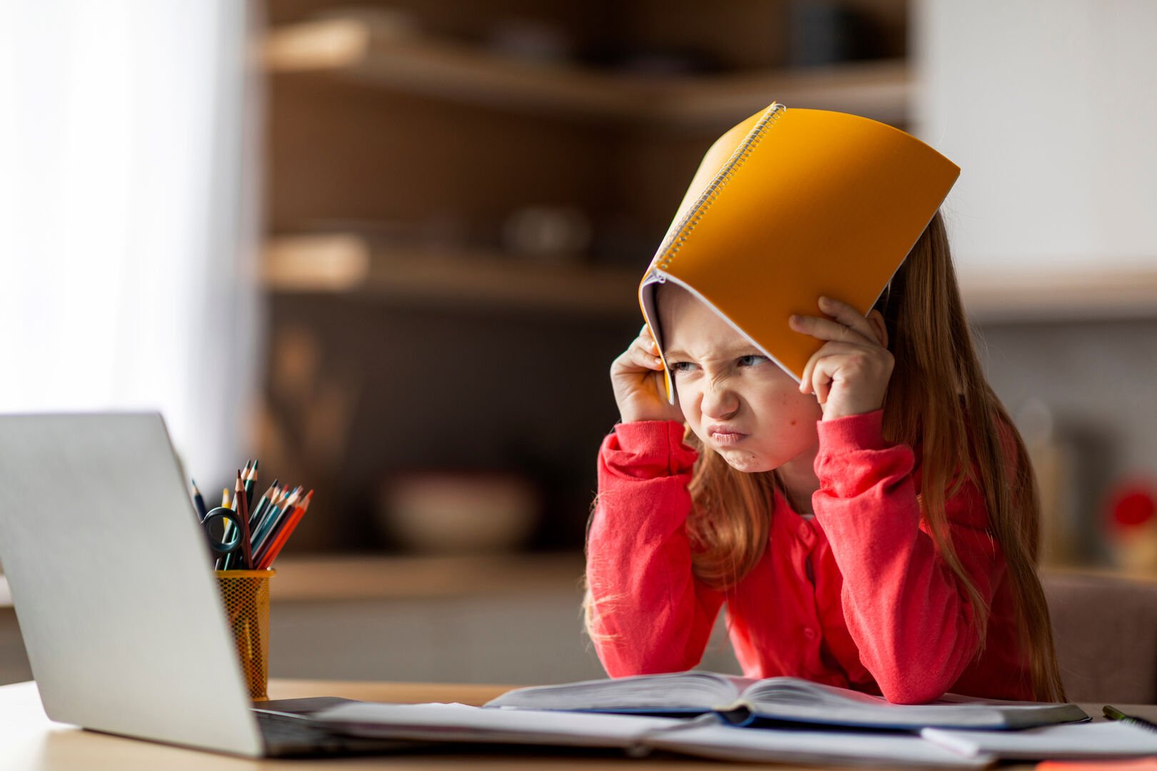 Learning Difficulties. Irritated Little Girl Covering Head With Workbook At Home