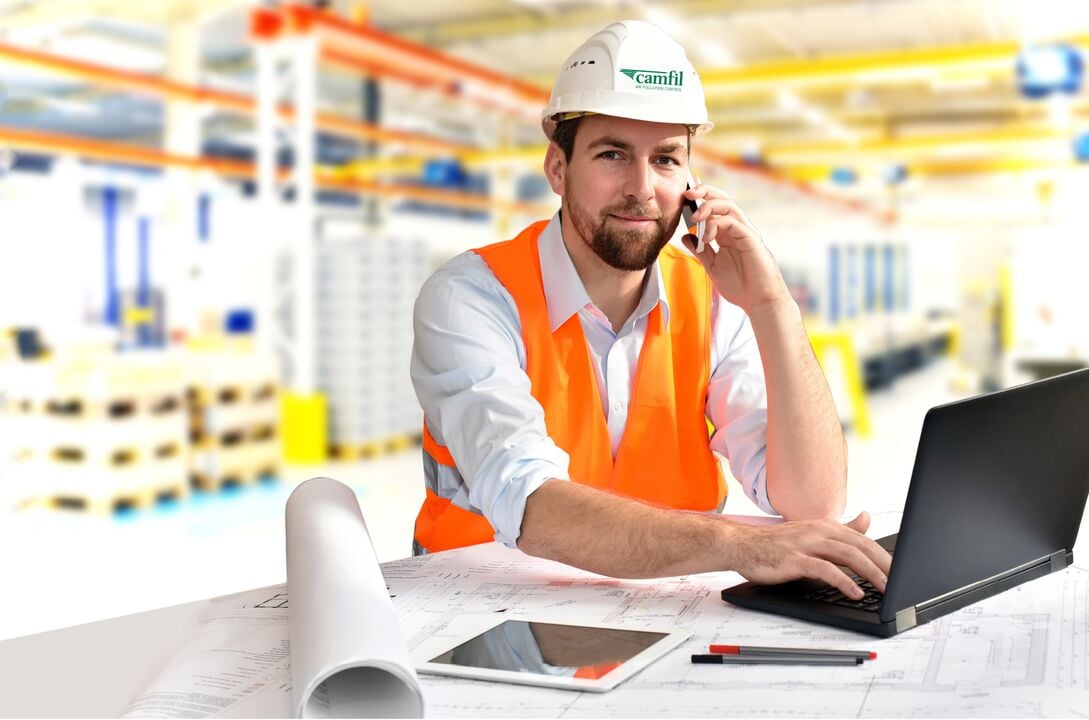 A Camfil service technician sitting at a desk with a laptop, talking on the phone