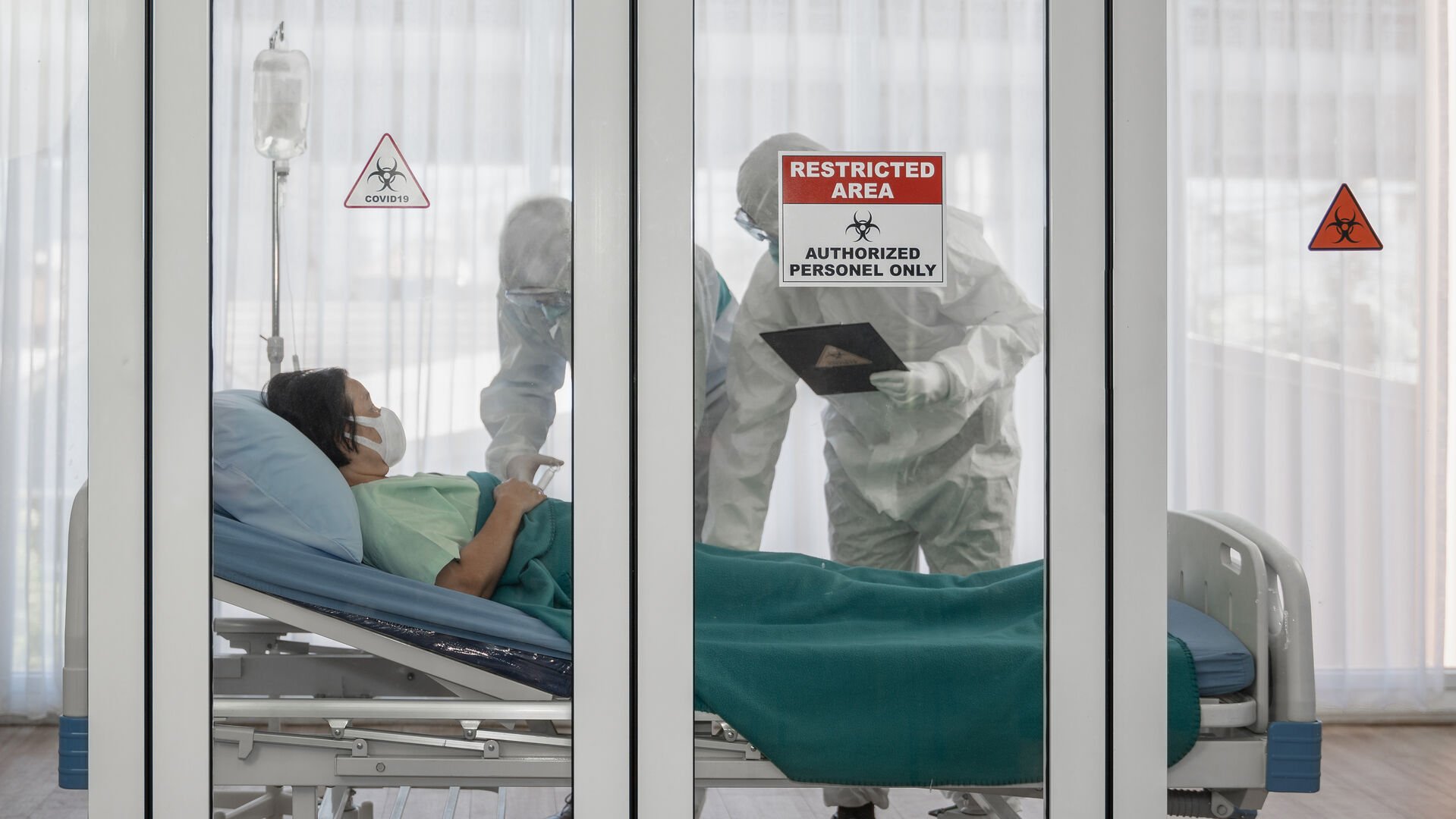 coronavirus covid-19 quarantine and breakout alert sign on window of quarantine room at hospital with disease control experts try to make disease treatment to infected patient who lying on bed