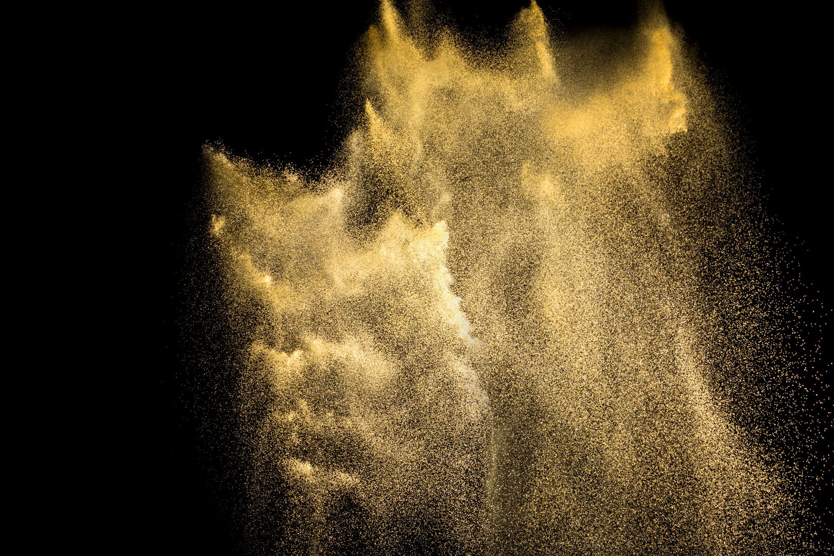 Golden sand explosion isolated on black background. Abstract sand cloud. Golden colored  sand splash agianst  dark background. Yellow sand fly wave in the air.
