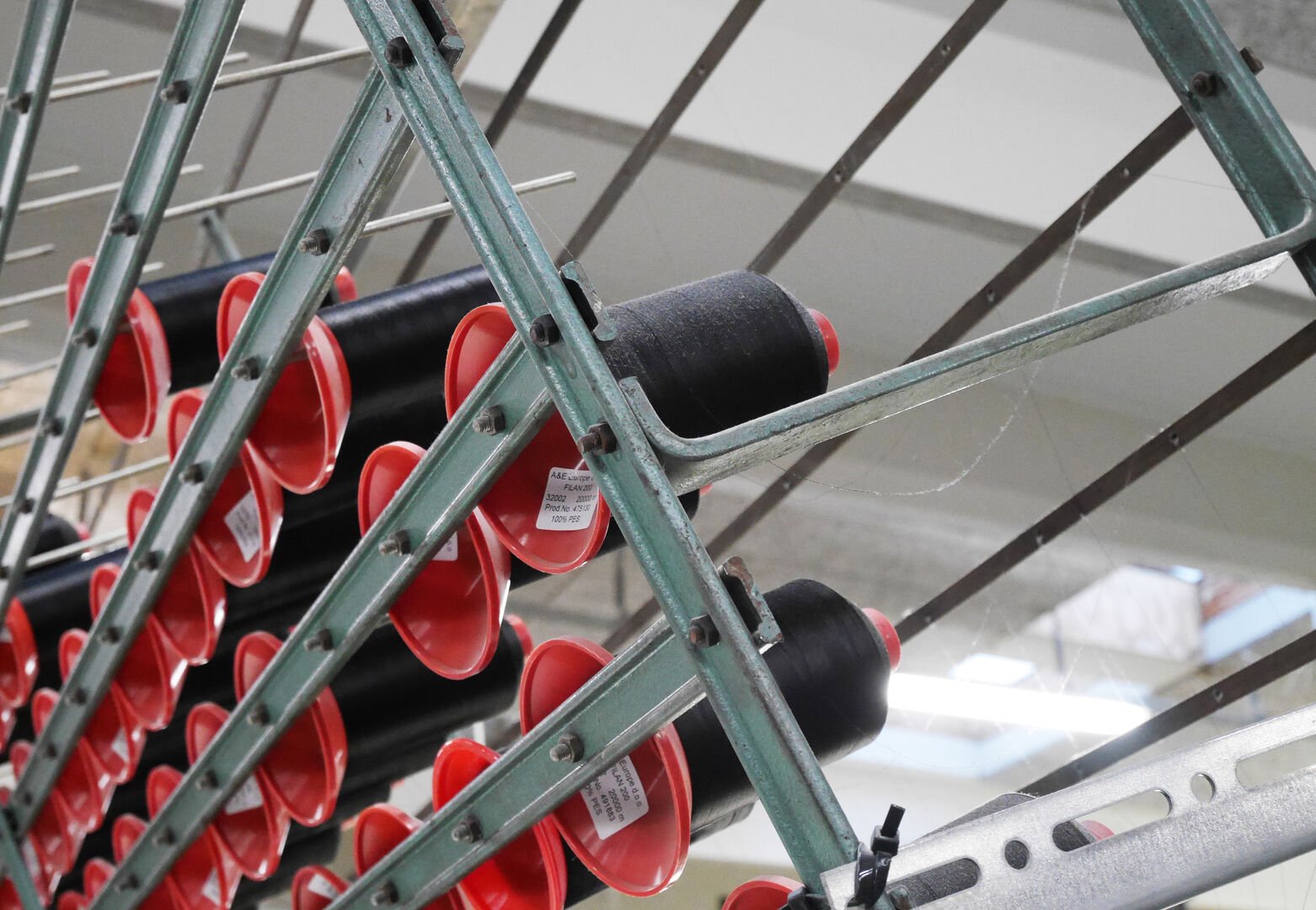 A rack displaying spools of black thread and red bobbins, arranged in a crisscross pattern