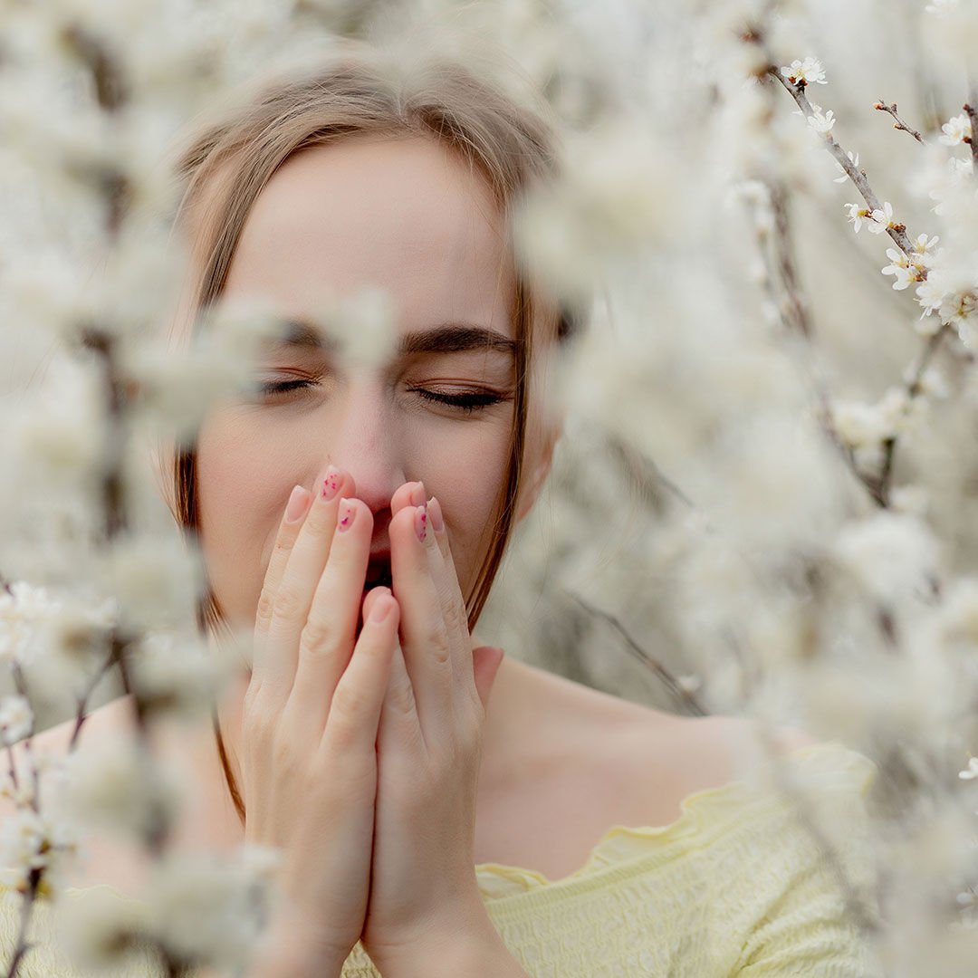 Young girl blowing nose and sneezing in tissue in front of blooming tree. Seasonal allergens affecting people. Beautiful lady has rhinitis